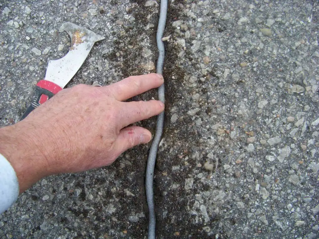 Foam backer rod installed in wide asphalt driveway crack before applying crack filler